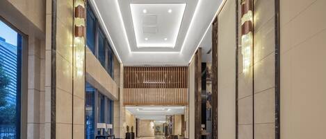 Un moderno vestíbulo de hotel con techo alto, iluminación empotrada y un panel de madera central.