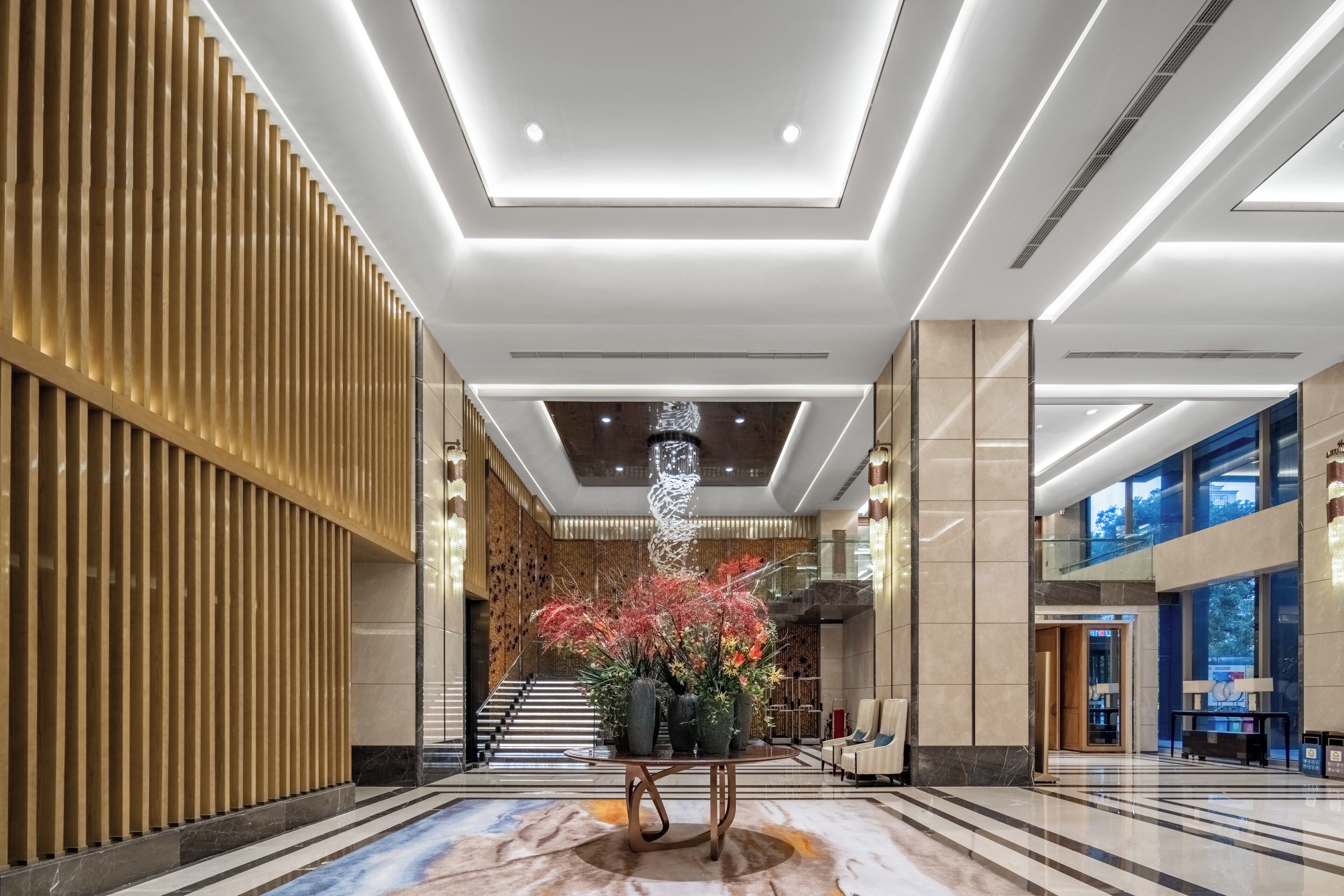 A modern lobby with a central floral arrangement, a staircase, and a seating area.