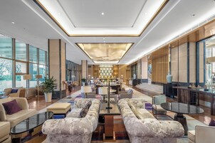 Un vestíbulo espacioso con una zona de estar central, ventanas amplias y un moderno candelabro.