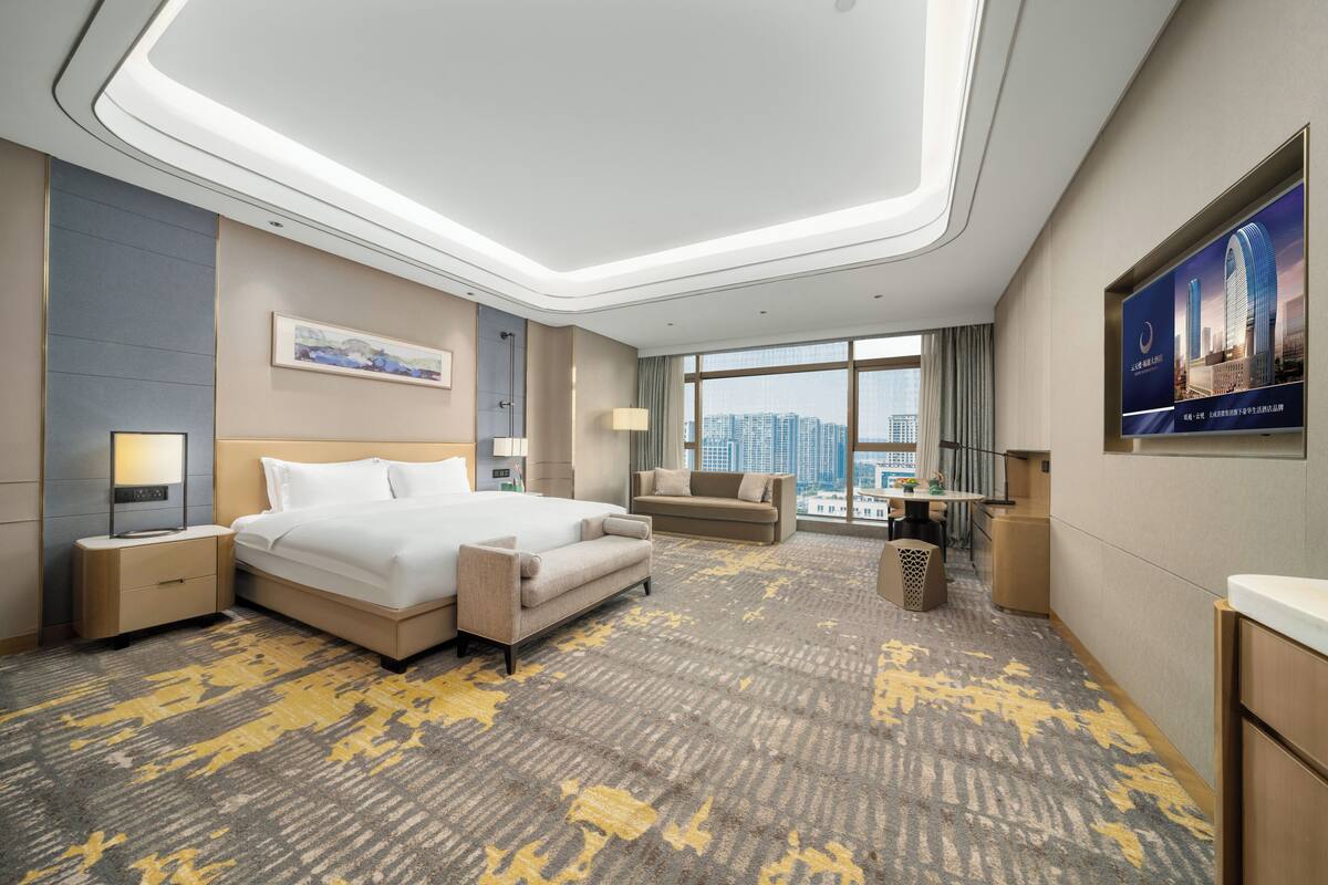 Habitación de hotel moderna con una cama grande, un escritorio, un sofá y vistas a la ciudad.