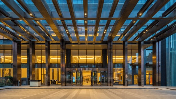 Un bâtiment moderne doté d’une façade en verre, de grandes portes d’entrée et d’un plafond au design structuré.