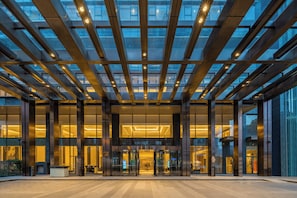 A modern building with a glass facade, large entrance doors, and a structured ceiling design.