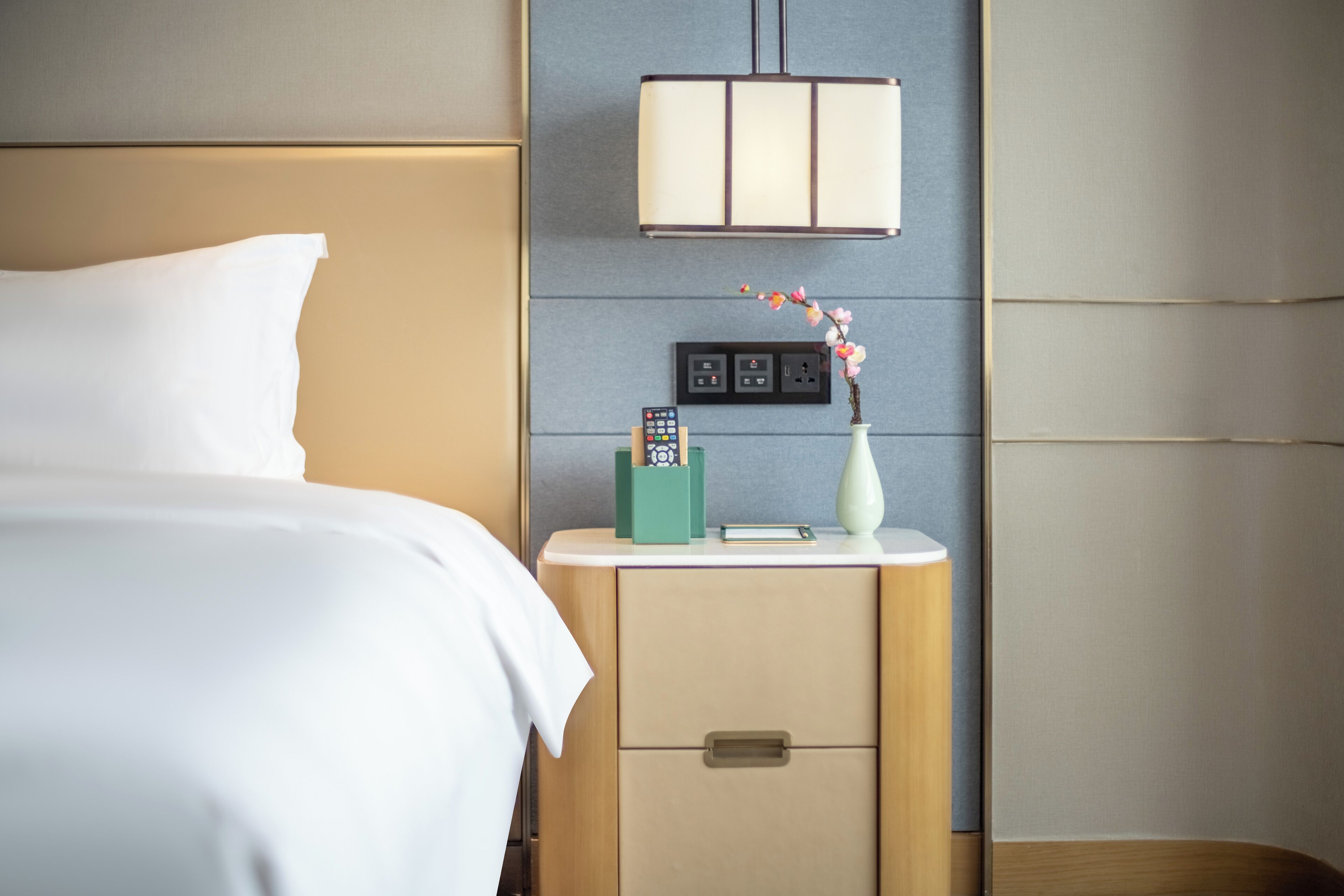 Une chambre d’hôtel bien rangée, avec un lit, une table de chevet, une lampe et un vase rempli de fleurs.