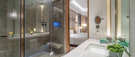 A modern bathroom with a glass-enclosed shower, a large mirror, and a vanity with a green plant.