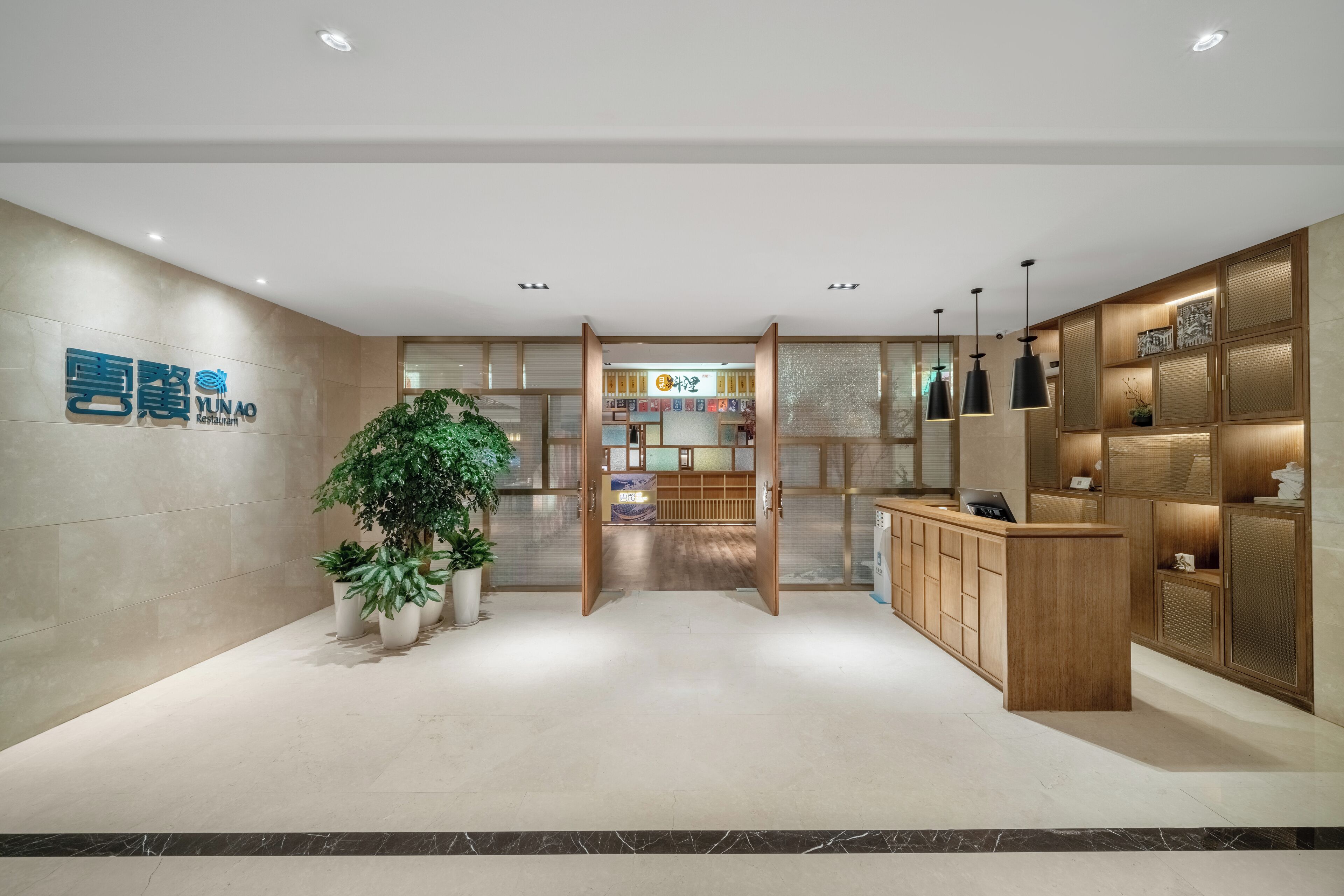 A modern hotel lobby with a reception desk, potted plants, and a wooden reception area.