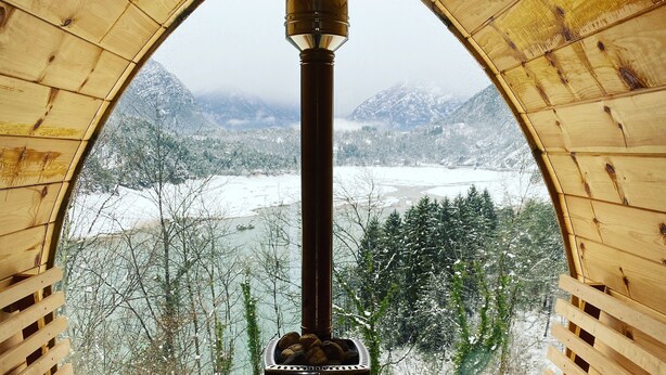 Una baita di legno con stufa a legna centrale, panche e vista su un paesaggio innevato.