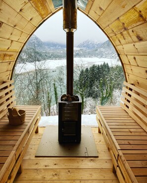 A wooden cabin with a central wood stove, benches, and a view of a snowy landscape. - Albergo Wellness da Febo (Tramonti di Sotto)