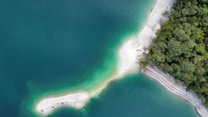 Vista aerea di una zona costiera con acque cristalline color turchese, una spiaggia sabbiosa e vegetazione lussureggiante.