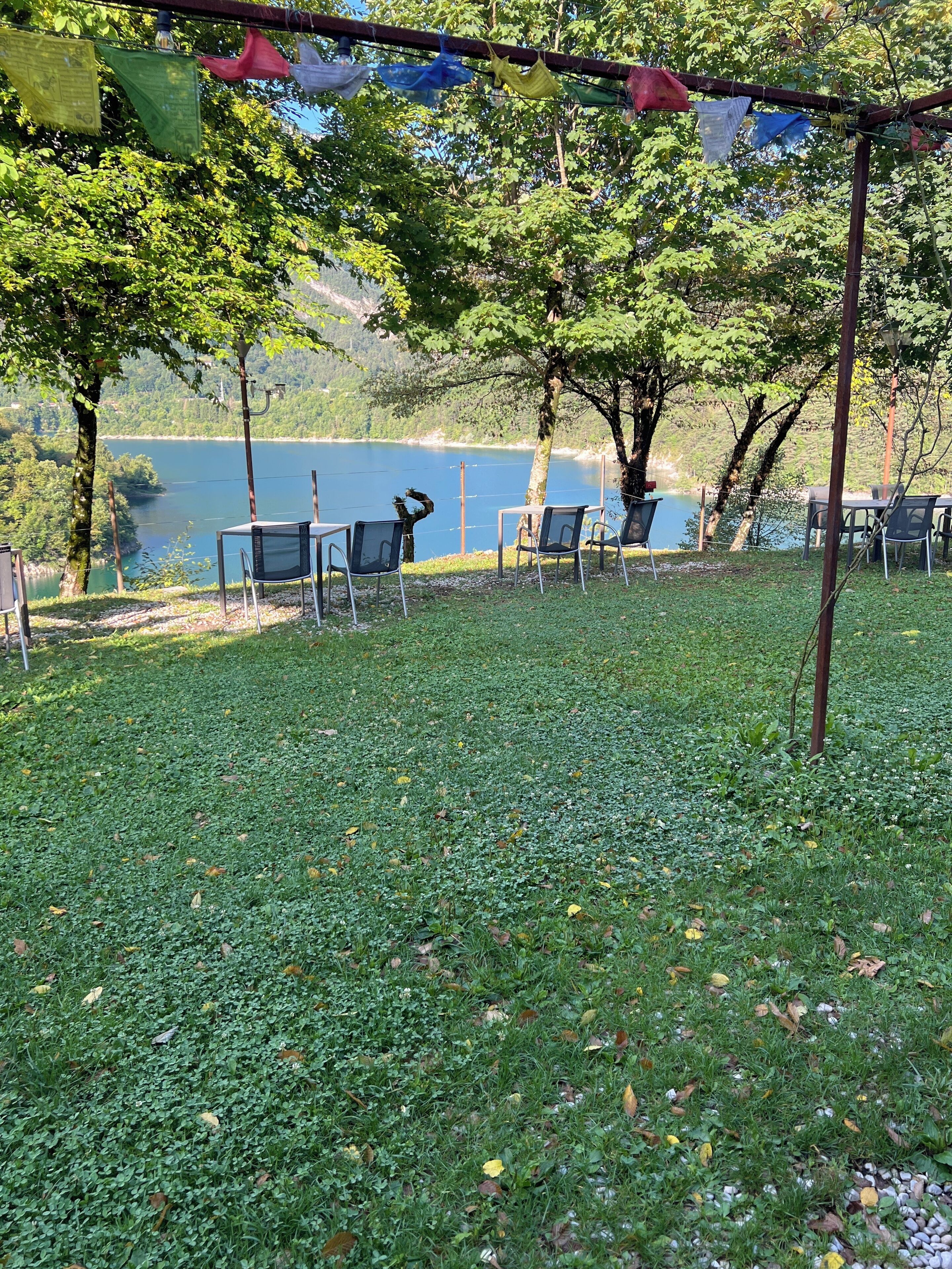 A serene outdoor seating area with tables and chairs, overlooking a lake and surrounded by trees.