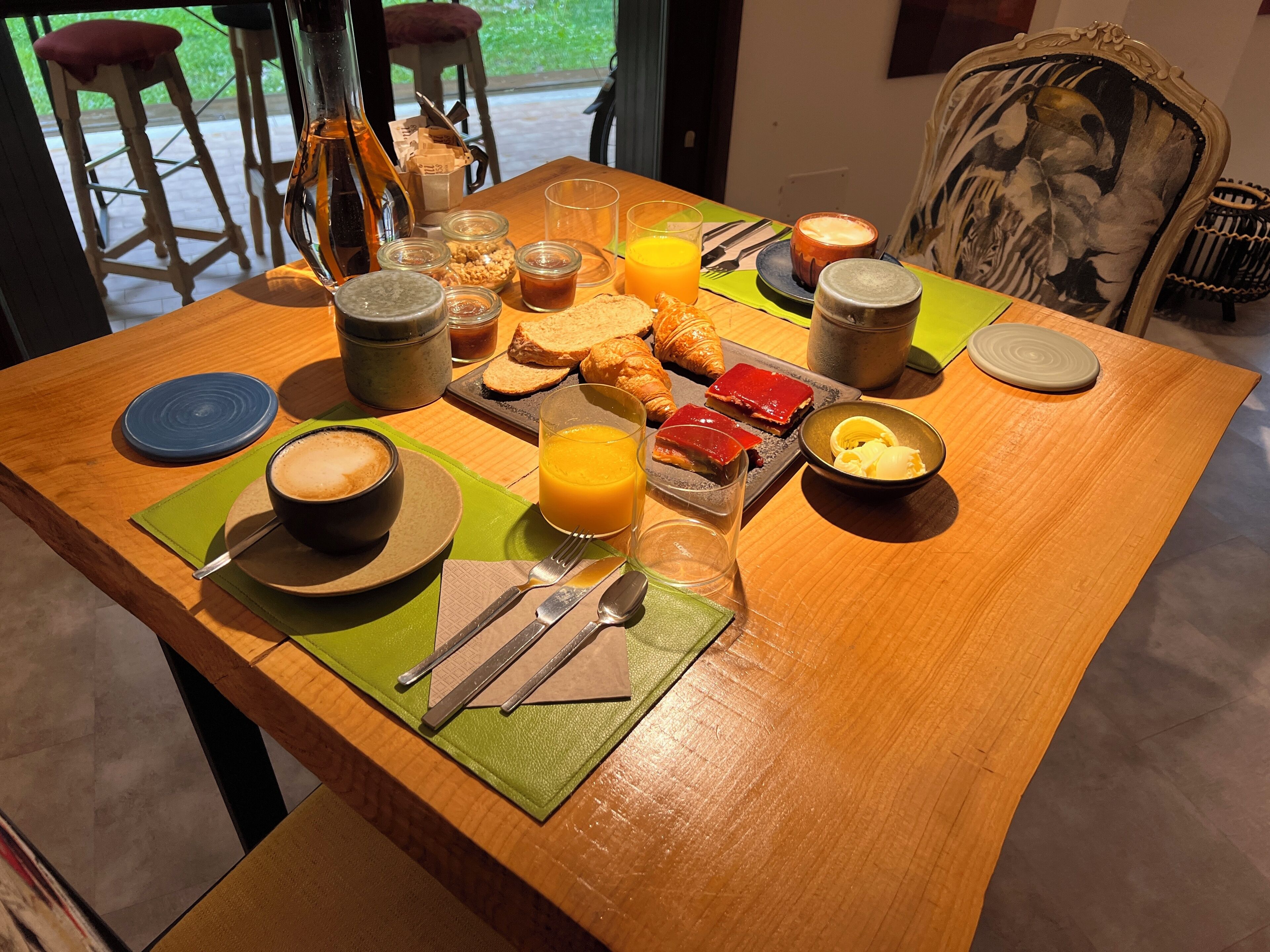 Mesa de desayuno servida con cruasanes, tostadas, mermelada, mantequilla y una taza de café.