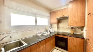 A kitchen with wooden cabinets, a stainless steel sink, a built-in oven, and a window above the sink. - Sunrise at Home by Gloove (El Campello)