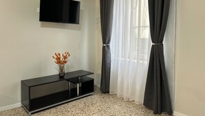 Ein modernes Wohnzimmer mit einem flachbildfernseher an der Wand, einem schwarzen Konsolentisch mit einer Vase und einem großen Fenster mit grauen Vorhängen.