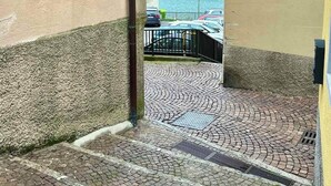 Ein Kopfsteinpflasterweg führt zu einem Wasserblick, mit geparkten Autos und einem Gebäude mit Holzläden.