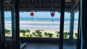 A beach view from a covered area with a wooden bench and red lanterns.