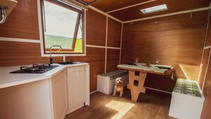 Une petite cuisine équipée d’un évier, d’une cuisinière et d’un chien assis près d’une table avec un banc.