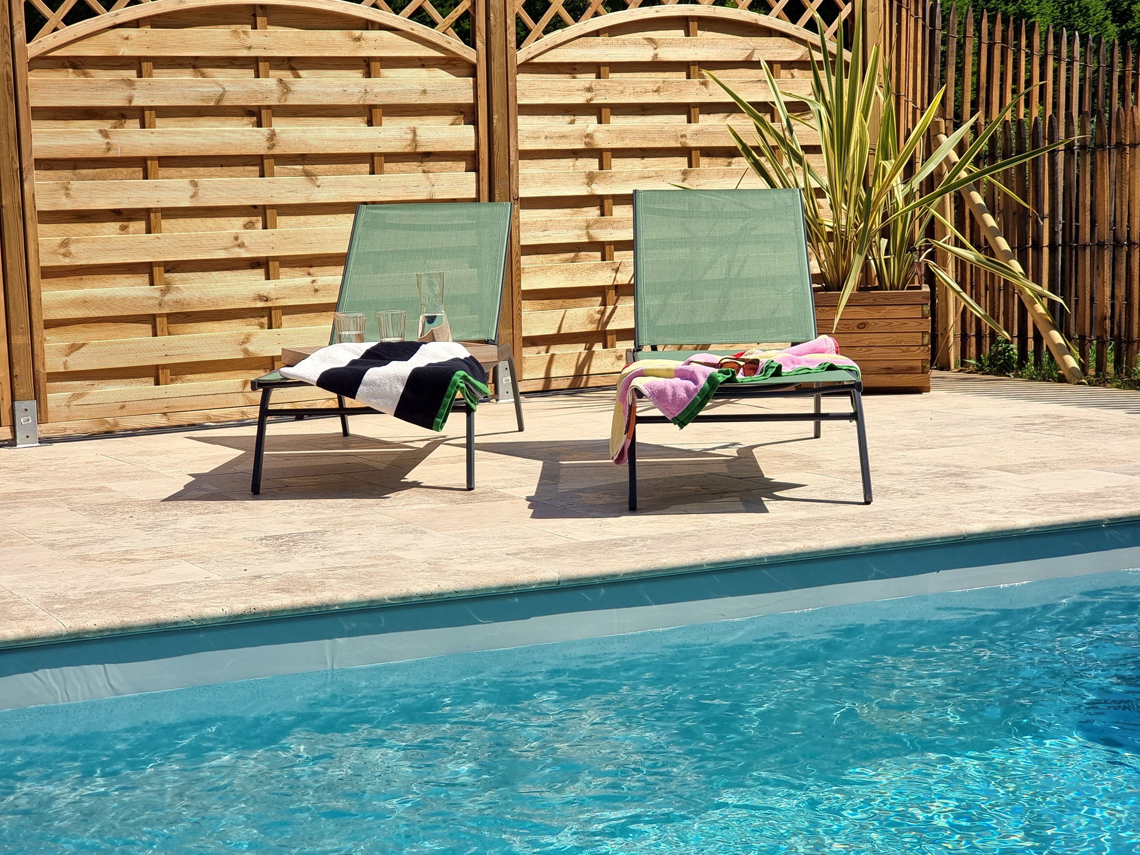 Dos sillones con toallas, una piscina y una valla de madera al fondo.