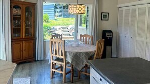 Ein Essbereich mit Tisch und Stühlen, einem Holzschrank, einer Hängeleuchte und Blick ins Freie.
