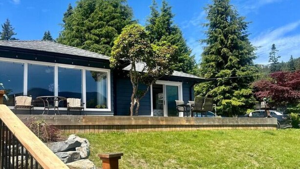 Ein modernes Haus mit großer Glasfront, einer Holzterrasse und einem gepflegten Rasen.