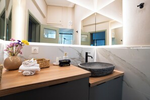 A bathroom with a wooden vanity, a marble sink, and a mirror reflecting the room. - Central, Modern & Sunny Apartment with city view! Pets & Family Friendly! (Tripoli)