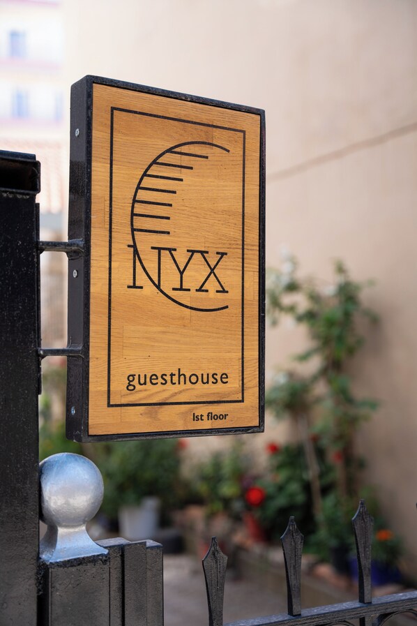 A wooden sign with a circular design and the letters 'NYX' above the word 'guesthouse' on the first floor. - Central, Modern & Sunny Apartment with city view! Pets & Family Friendly! (Tripoli)