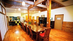 A spacious dining area with a long wooden table and chairs, a kitchen in the background, and a wooden ceiling structure. - Minsyuku yuinoie (Tatsugo)