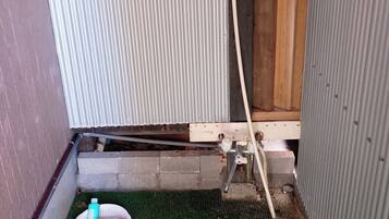 A small, enclosed bathroom with a shower area, a green mat, and a basin with toiletries.