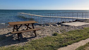 Une table de pique-nique en bois et une plateforme en béton au bord de la mer, avec une rambarde en métal.