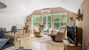 Un salon spacieux avec un plafond haut, de grandes fenêtres, un téléviseur à écran plat et un coin salon confortable.