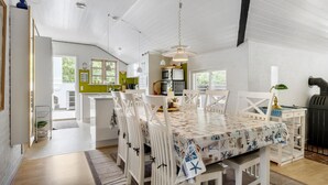 Une cuisine spacieuse avec des meubles blancs, un coin repas agrémenté d’une nappe à motifs et une vue sur l’extérieur grâce à de grandes fenêtres.