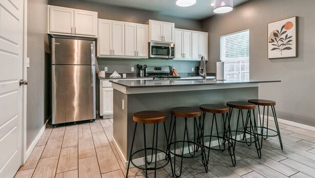 Una cocina moderna con armarios blancos, electrodomésticos de acero inoxidable y una zona de bar con taburetes.