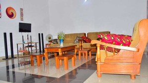 Ein Wohnzimmer mit einer Couch, einem Holztisch und Sesseln. An der Wand ist ein Fernseher angebracht und ein dekoratives Wandbild zu sehen.