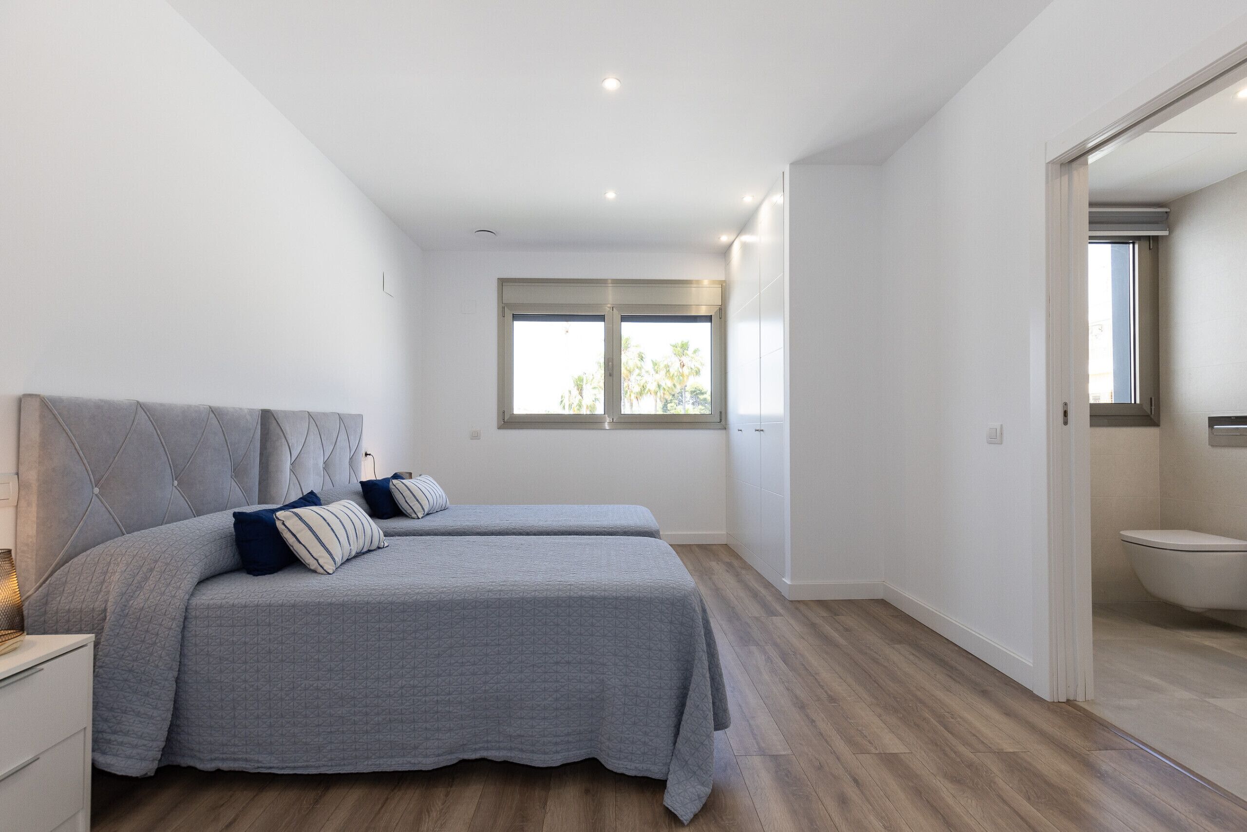 A bedroom with two beds, a window, and a bathroom visible through an open door.