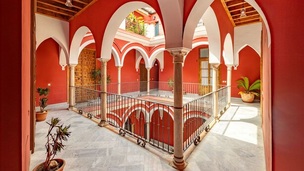 Un patio con paredes rojas, arcos blancos y suelo de baldosas.