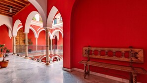Un patio interior con paredes rojas, arcos blancos y un banco de madera.