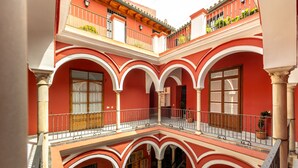 Un patio de varios niveles con paredes rojas, arcos blancos y balcones con plantas.