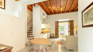 Amplia sala de estar con techo de madera, una mesa de comedor con sillas, un sofá y una escalera que sube a un nivel superior.