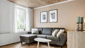 Moderni olohuone, jossa on harmaa kulmasohva, pieni valkoinen sivupöytä ja kaksi kehystettyä kuvaa seinällä.