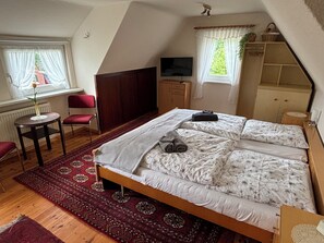 A bedroom with a bed, a desk, a chair, a TV, and a window with curtains. - Reetgedecktes Ferienhaus am Strandweg (Lütjensee)