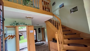 Une pièce spacieuse avec un escalier en bois, une porte en bois portant une inscription et une vue sur l’extérieur.