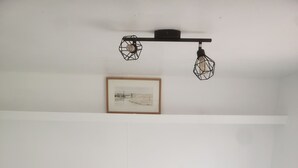 Un dormitorio con cama, dos almohadas, un cuadro enmarcado en la pared y una lámpara en el techo.