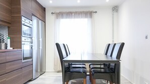 Une cuisine moderne dotée d’appareils électroménagers intégrés, une table à manger avec des chaises et une grande fenêtre agrémentée de rideaux.