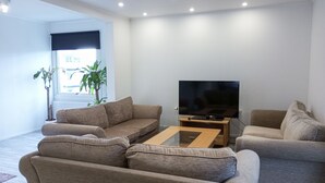 Un salon moderne avec un grand téléviseur à écran plat posé sur un meuble en bois, deux canapés beige et une table basse en verre.