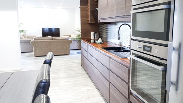 Une cuisine moderne dotée d’appareils électroménagers en acier inoxydable, de meubles en bois et d’un four encastré.