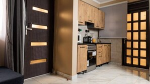 A compact kitchen with wooden cabinets, a built-in oven, and a window with a grid pattern. - Fed Stay Naalya (Kampala)