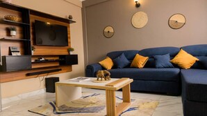 A living room with a blue sofa, wooden shelves, a flat-screen TV, and decorative wall art. - Fed Stay Naalya (Kampala)