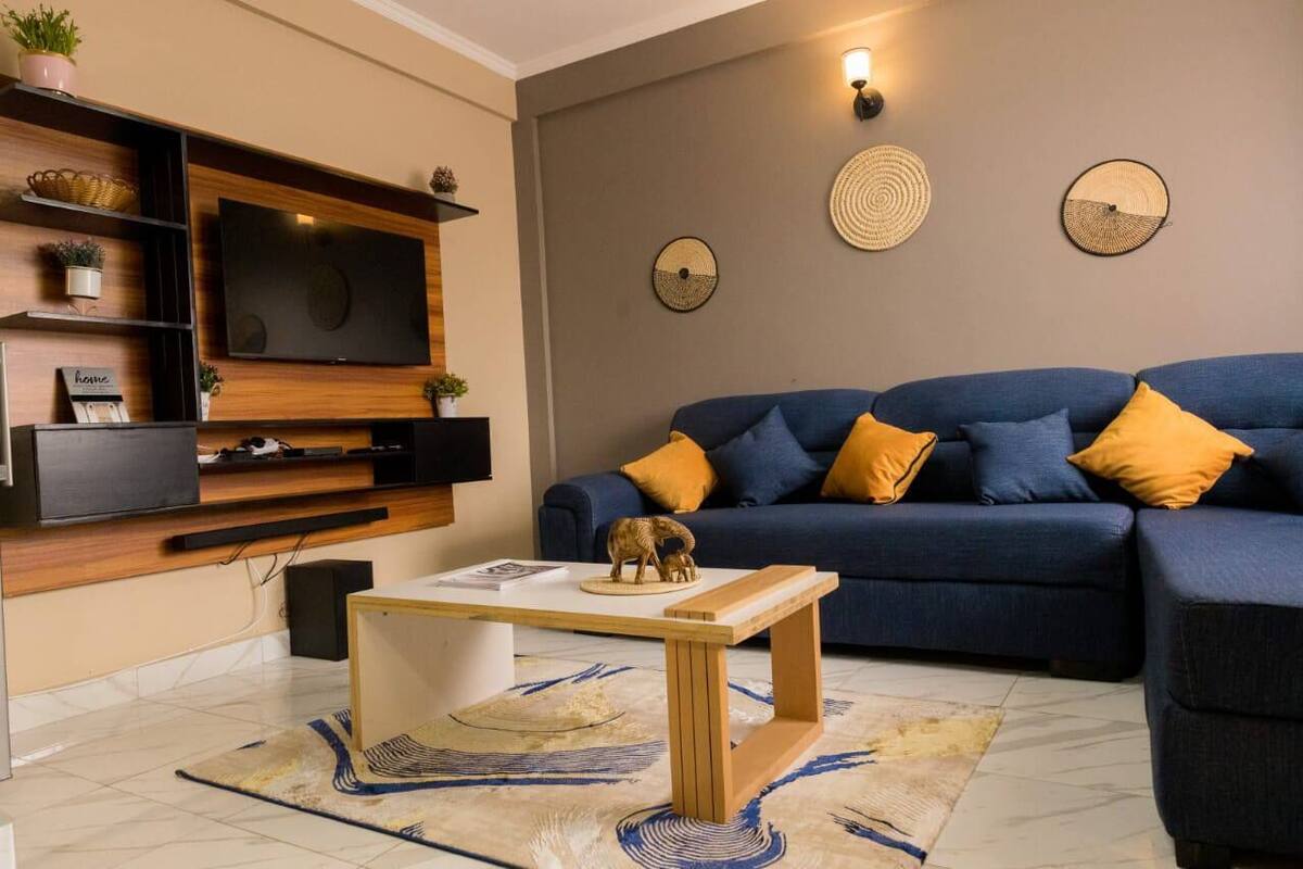A living room with a blue sofa, wooden shelves, a flat-screen TV, and decorative wall art.
