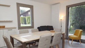 Un'area pranzo moderna con un tavolo e sedie in legno, una sedia nera, una sedia gialla e vista sul verde attraverso una grande finestra.