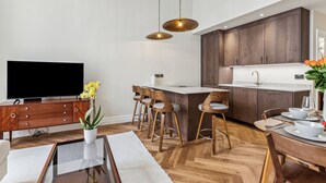A modern kitchen with wooden cabinets, a central island with bar stools, a dining table with chairs, and a flat-screen TV on a wooden cabinet. - Idyllic Notting Hill 2Bed 2Bath Apartment (London)
