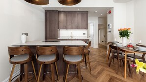 A modern kitchen with wooden cabinets, a central island with bar stools, pendant lighting, and a dining area with a table and chairs. - Idyllic Notting Hill 2Bed 2Bath Apartment (London)
