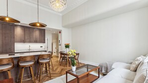 A modern kitchen with wooden cabinets, a central island with stools, and a dining area with a table and chairs. - Idyllic Notting Hill 2Bed 2Bath Apartment (London)